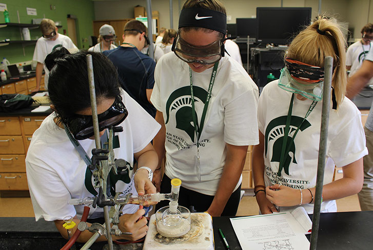 Three students attending the summer program, hovering over a beaker