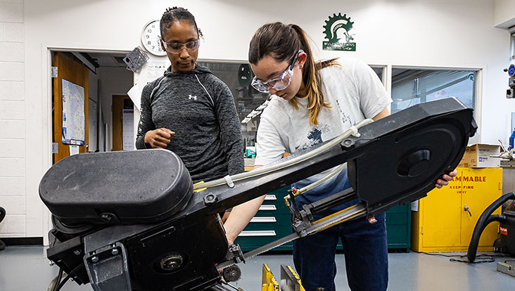Students working on a heavy cutting machine in a workshop